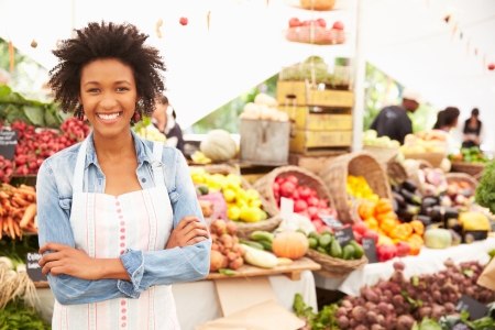 Female Stall Holder At Farmers Fresh Food Market, Smiling To Camera